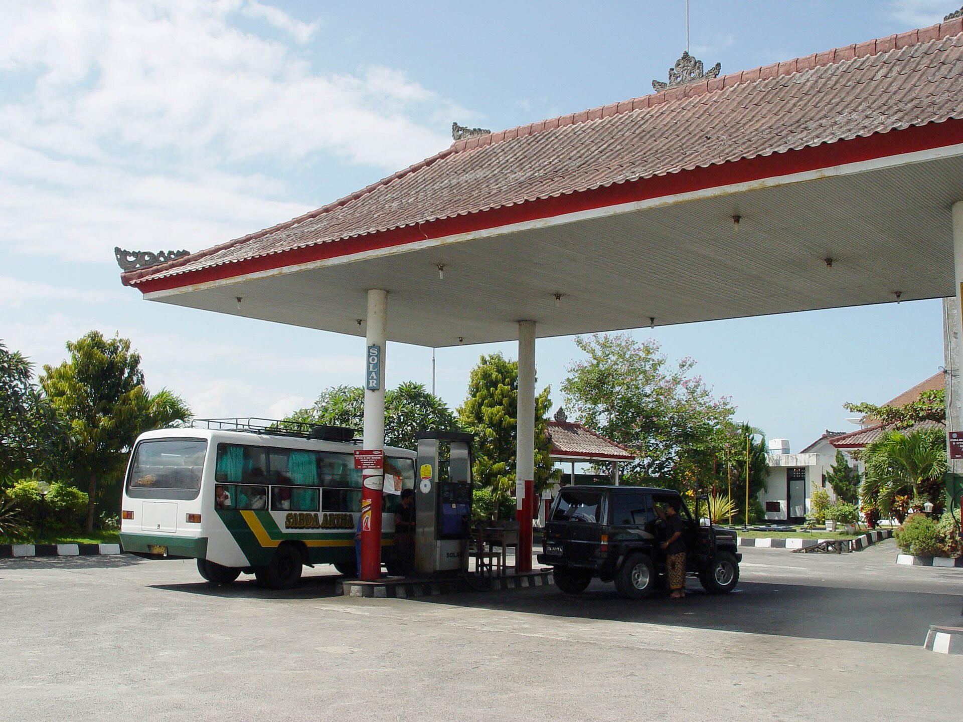 A Balinese-style petrol station canopy in Batuan, Bali, with a bus and car at the pumps
