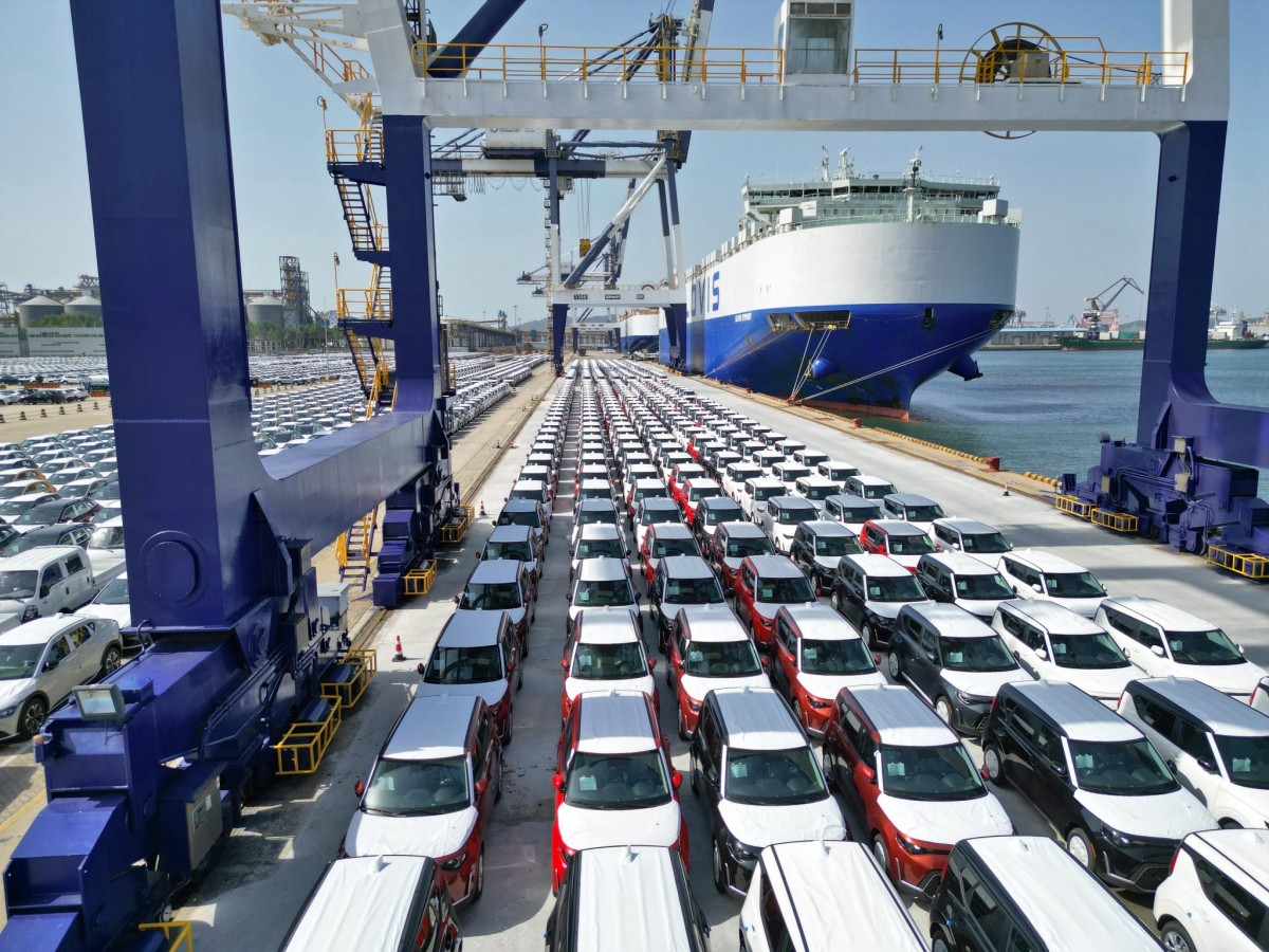 Rows of Chinese-made cars at an export terminal beside a vehicle carrier