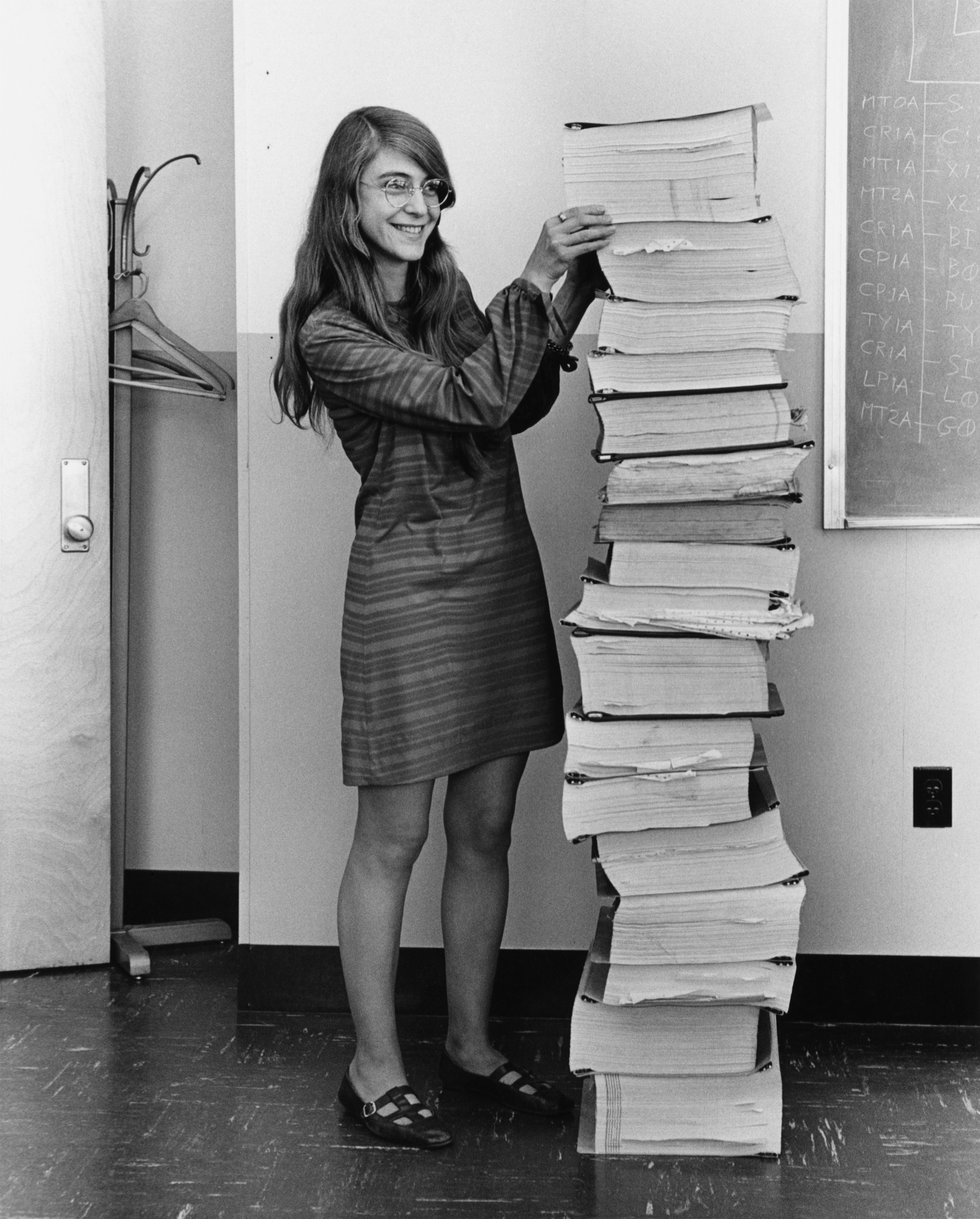 Margaret Hamilton in 1969 standing beside the stack of Apollo Guidance Computer source-code printouts produced by her MIT team