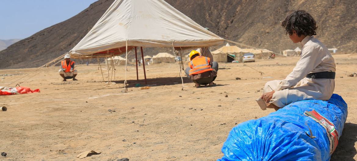 A displaced Yemeni child watches IOM workers erect emergency shelter during the Yemen displacement crisis