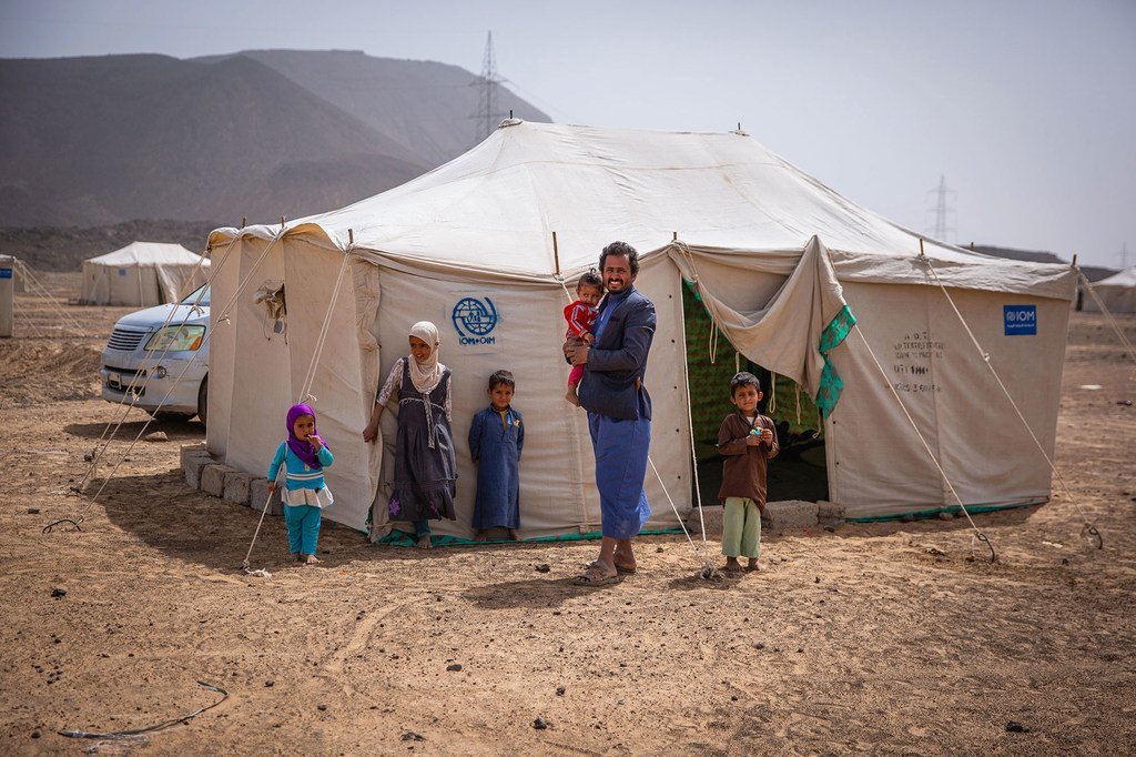 A displaced family stands outside an IOM shelter in Yemen during an earlier wave of displacement