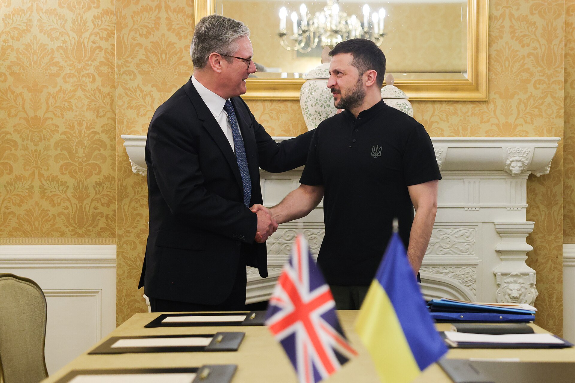 President Volodymyr Zelenskyy shaking hands with a British prime minister at a UK-Ukraine meeting in London, UK and Ukrainian flags on the table