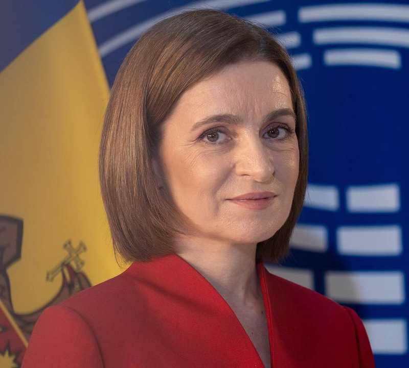 Moldovan President Maia Sandu in a red jacket before the Moldovan and European flags