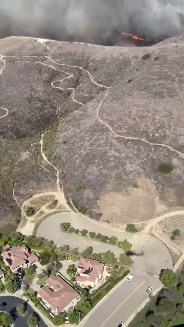 A line of flame crosses a ridge directly above homes at the edge of San Juan Capistrano during the Norte Fire