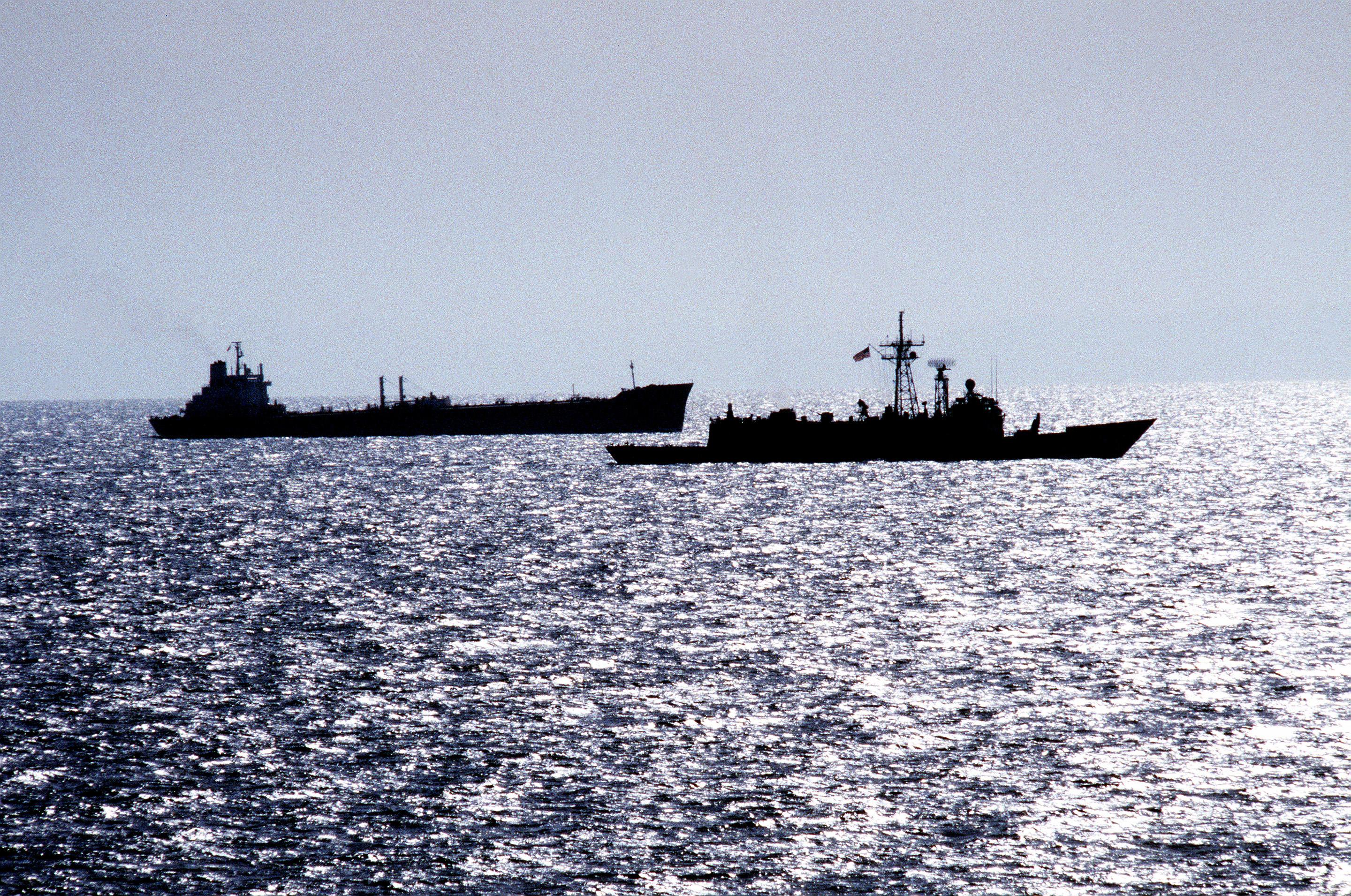 A U.S. Navy frigate escorts a reflagged tanker through the Persian Gulf at dusk during the Tanker War era — file photo