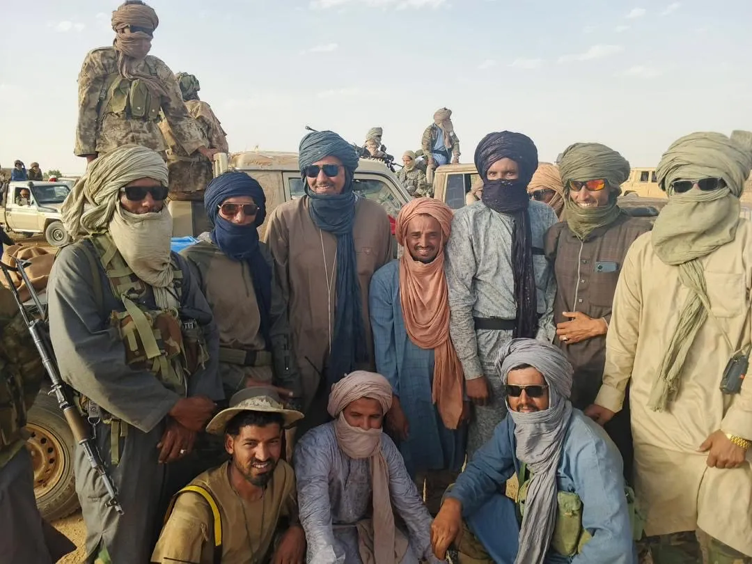 Armed fighters riding motorcycles across sandy ground in Mali