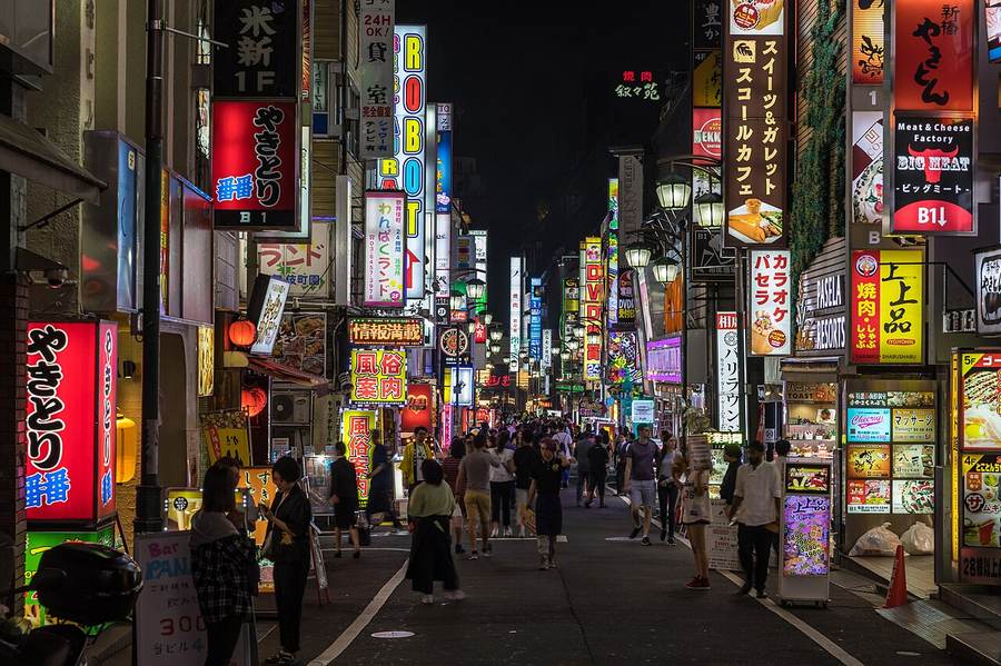 Pedestrians beneath Japanese-language signs in Tokyo's Kabukicho district as Japan raises permanent residency and renewal fees