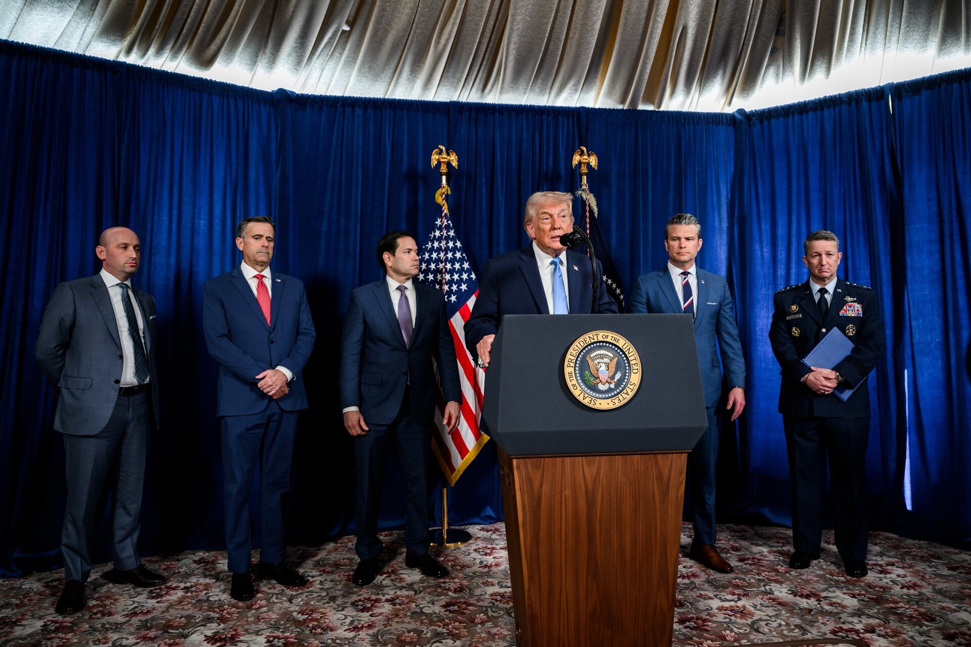 President Donald Trump speaking at a podium with the presidential seal, flanked by senior officials, in January 2026