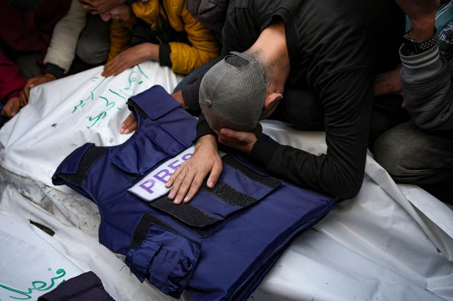 A grieving relative rests his hand on a PRESS vest laid over the body of a Palestinian journalist killed in Gaza