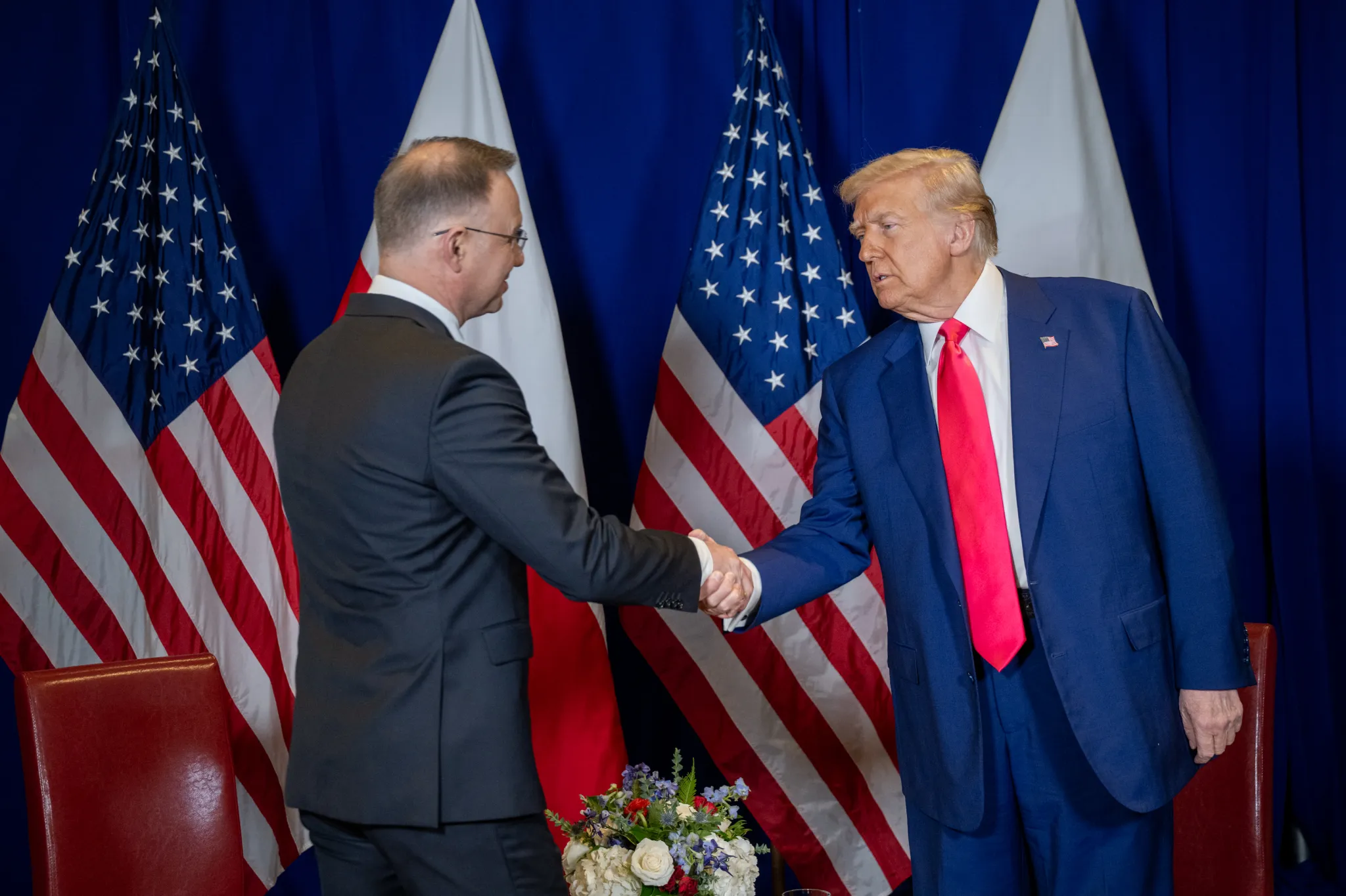 President Donald Trump and Polish President Andrzej Duda shake hands between United States and Polish flags