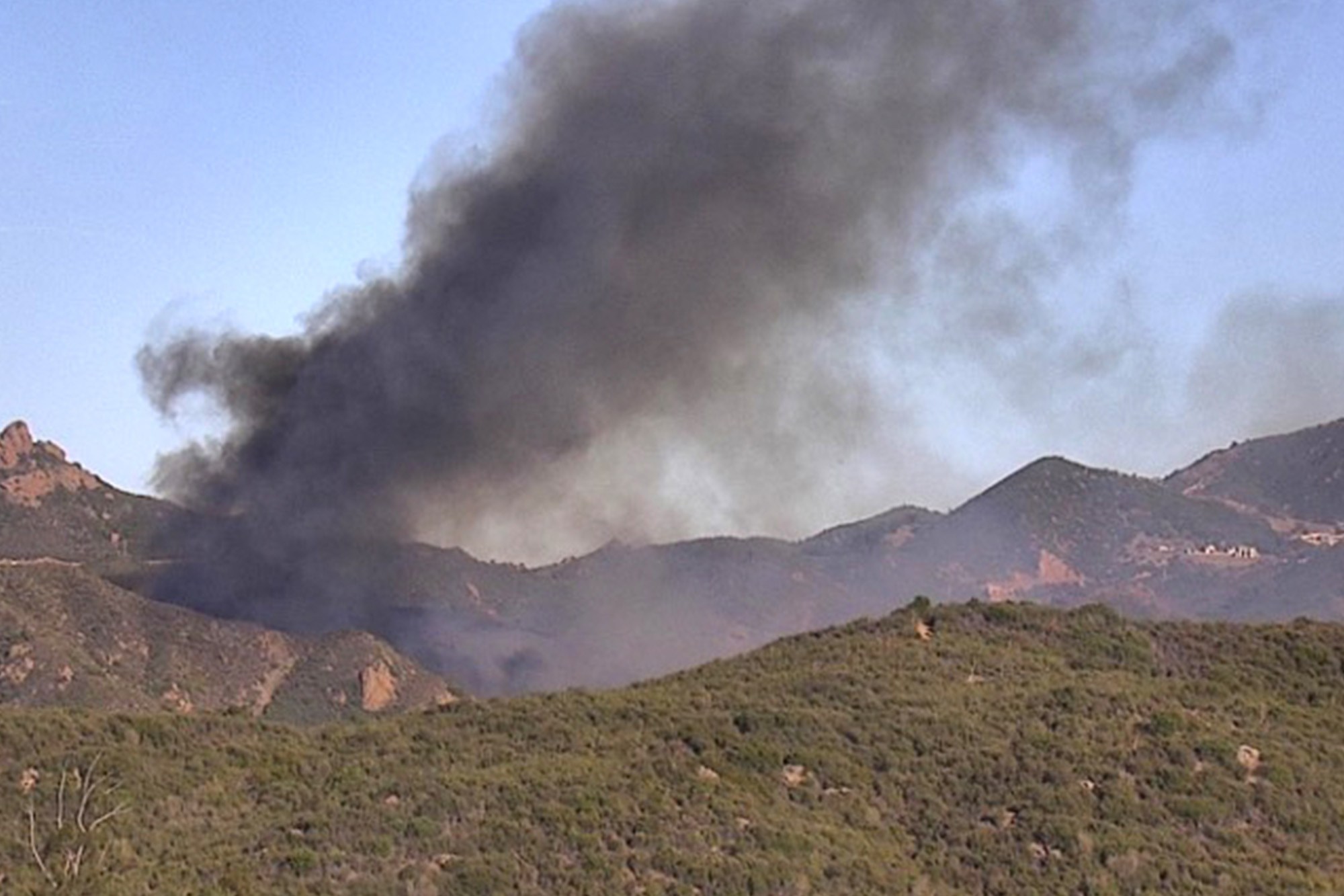 A thick column of dark smoke rises over the hills of western Malibu from the Bryson Fire on Thursday afternoon