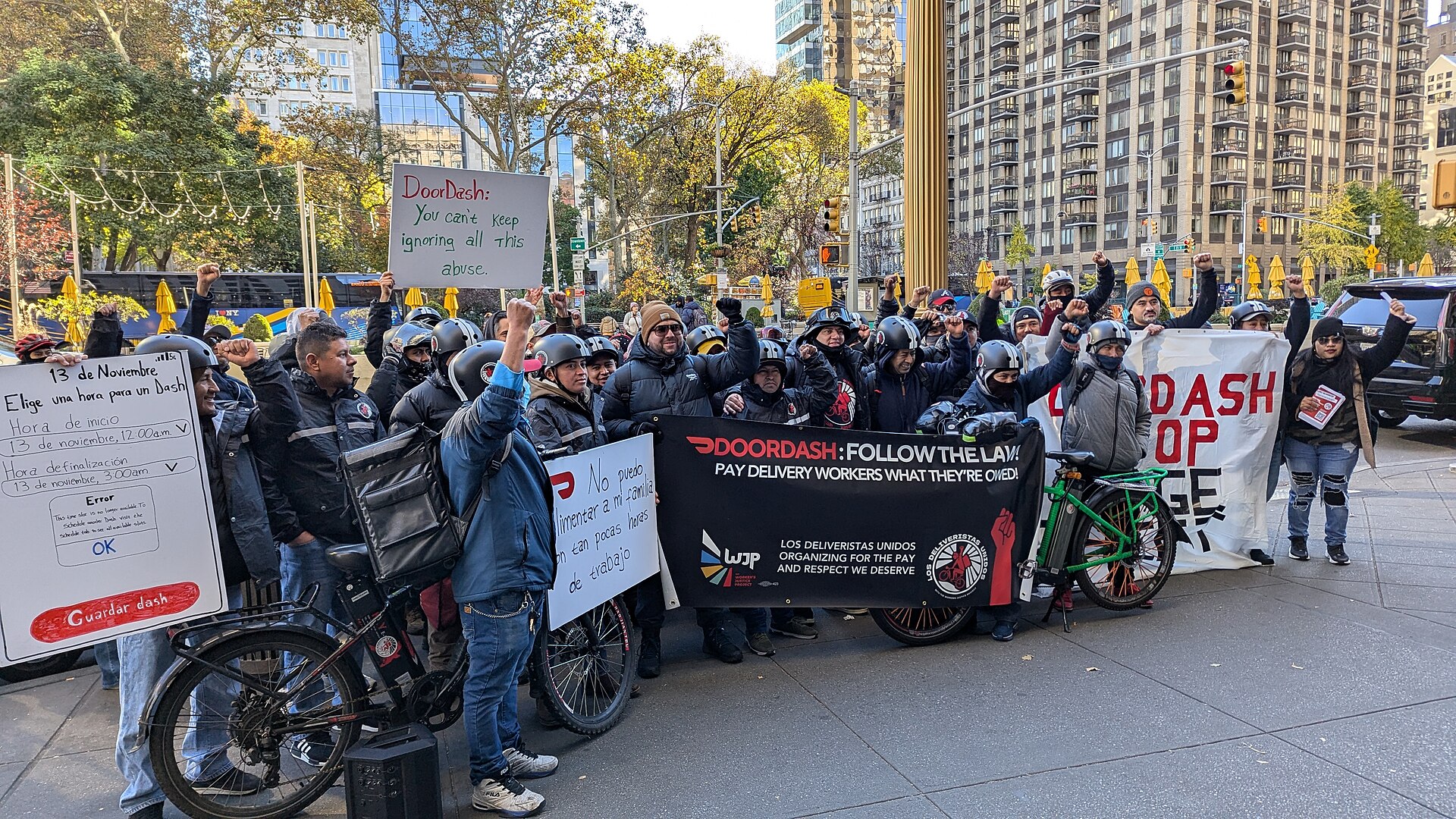 Members of Los Deliveristas Unidos, New York delivery workers, rally with bicycles and a banner reading 'DoorDash: follow the law — pay delivery workers what they're owed'