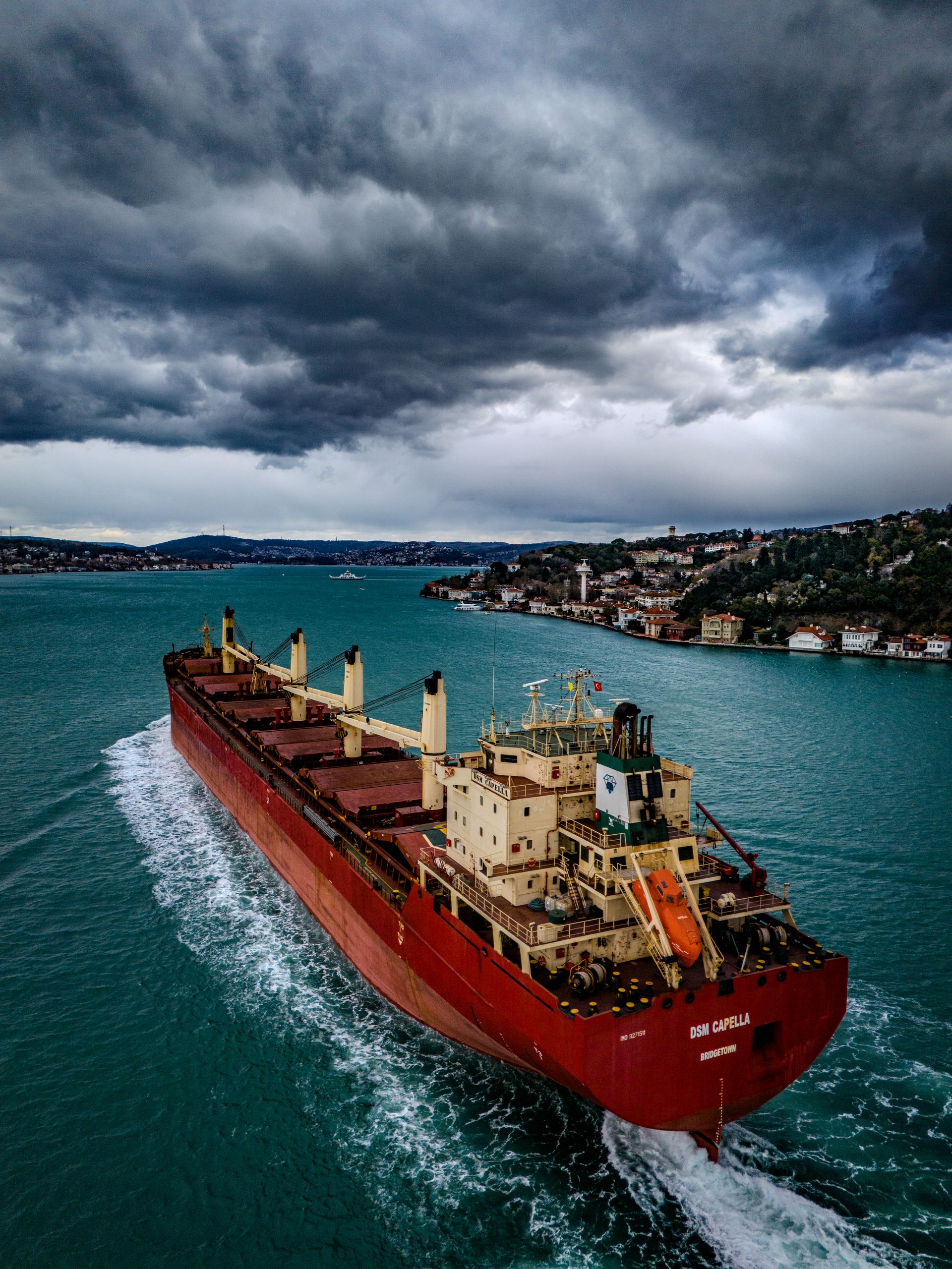 A bulk carrier transiting a narrow strait under storm clouds — the Black Sea blockade is squeezing Ukraine's grain export corridor