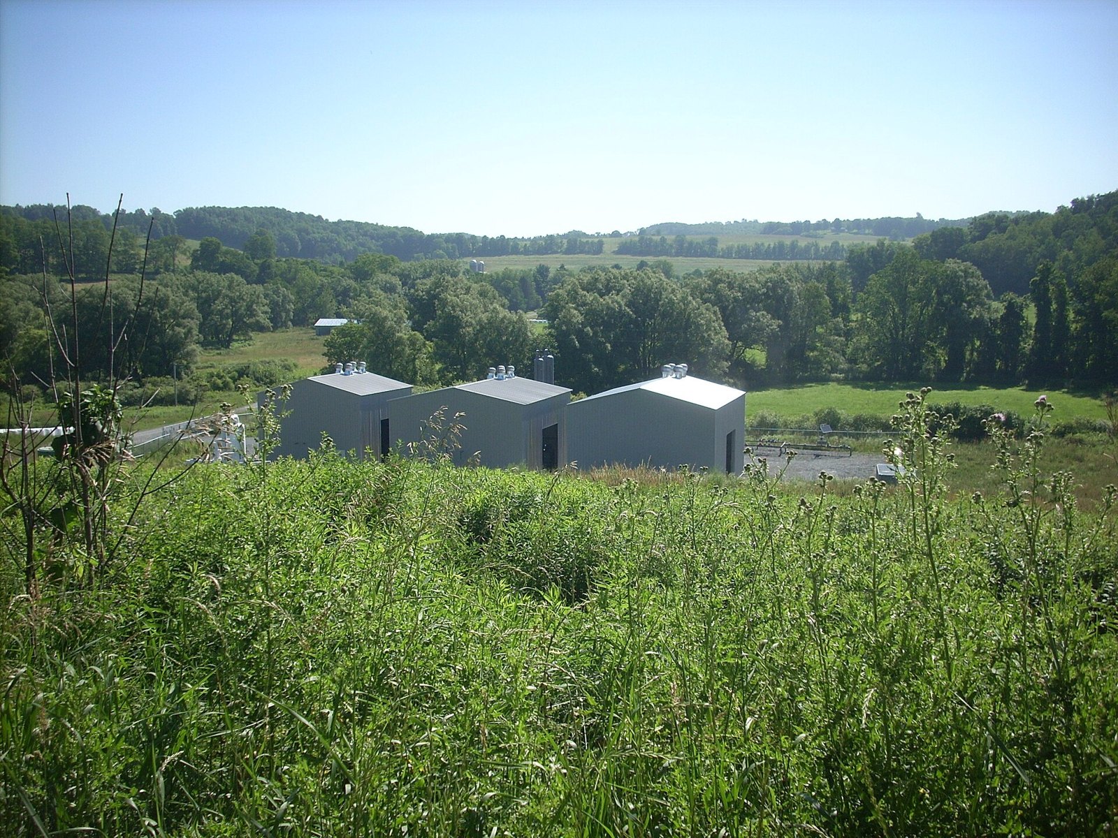 Natural gas compressor buildings in a green Appalachian valley, part of the midstream network behind the EQT Range Resources merger