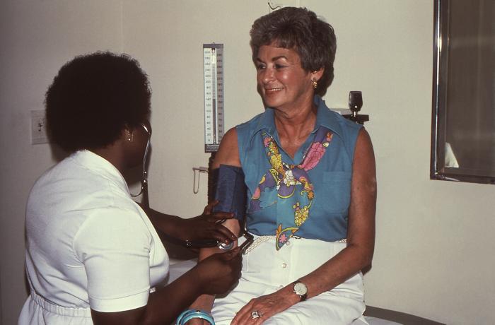 A health worker checks a patient's blood pressure in a clinic, illustrating routine preventive care that emergency-only Medicaid does not cover