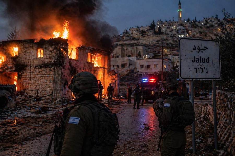 A building burns in Jalud during a settler arson attack earlier in 2026, with the Jalud road sign and Israeli forces visible