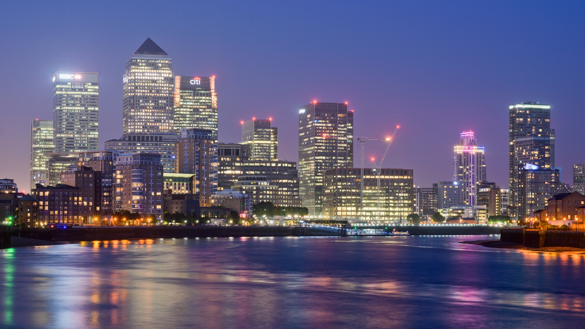 Canary Wharf financial district in London at dusk seen across the Thames from Limehouse, with the HSBC and Citi towers lit and One Canada Square's pyramid roof in the centre