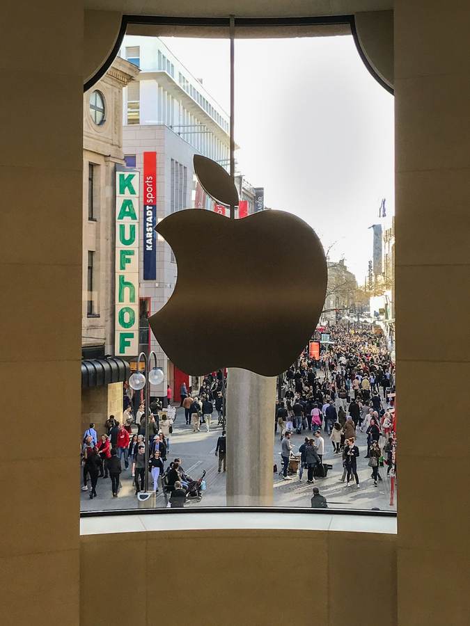 Apple logo on the glass facade of the Apple Store in Cologne, Germany, overlooking a busy shopping street