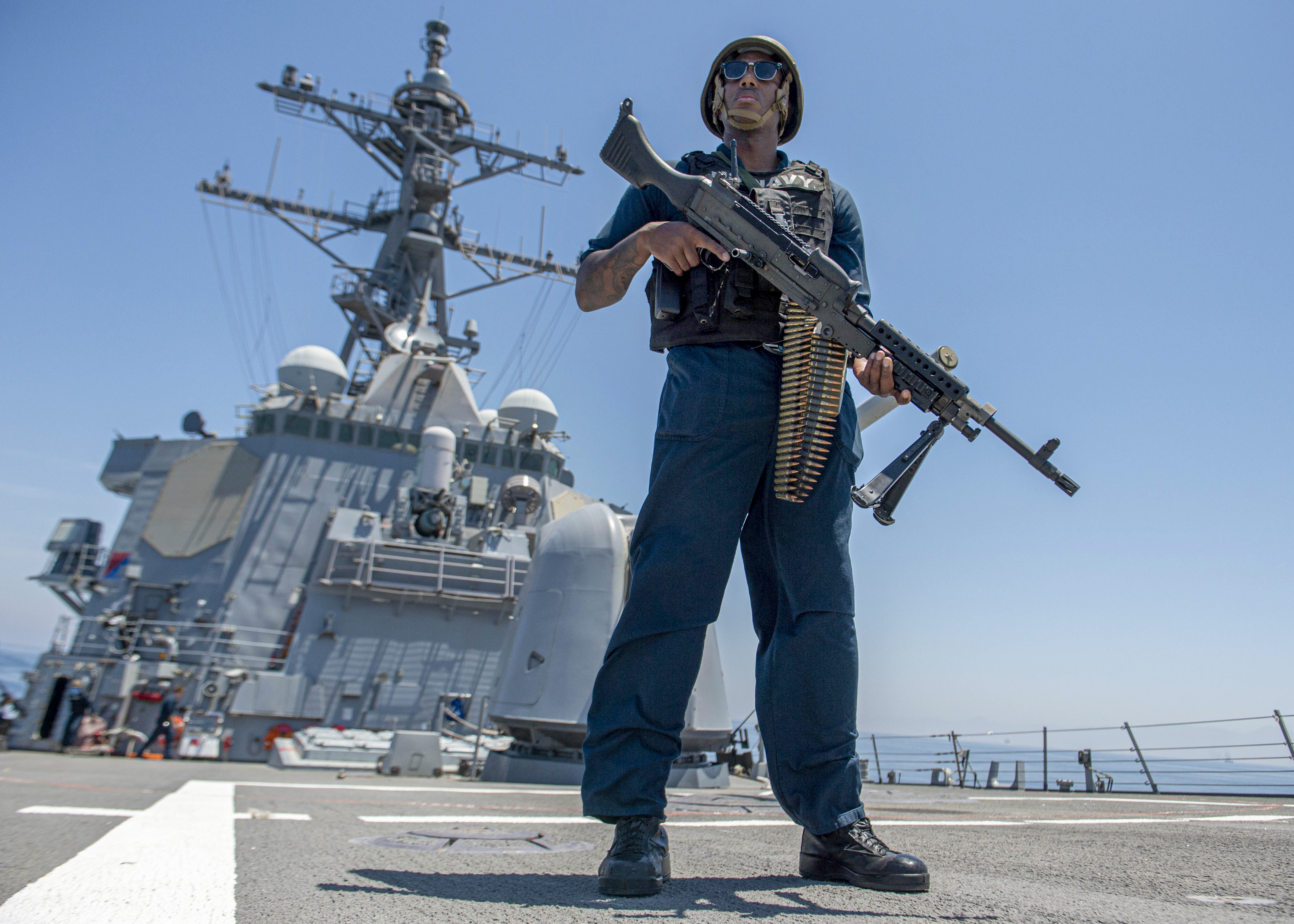 A U.S. Navy sailor stands watch with a machine gun on the deck of a warship during a Strait of Hormuz transit