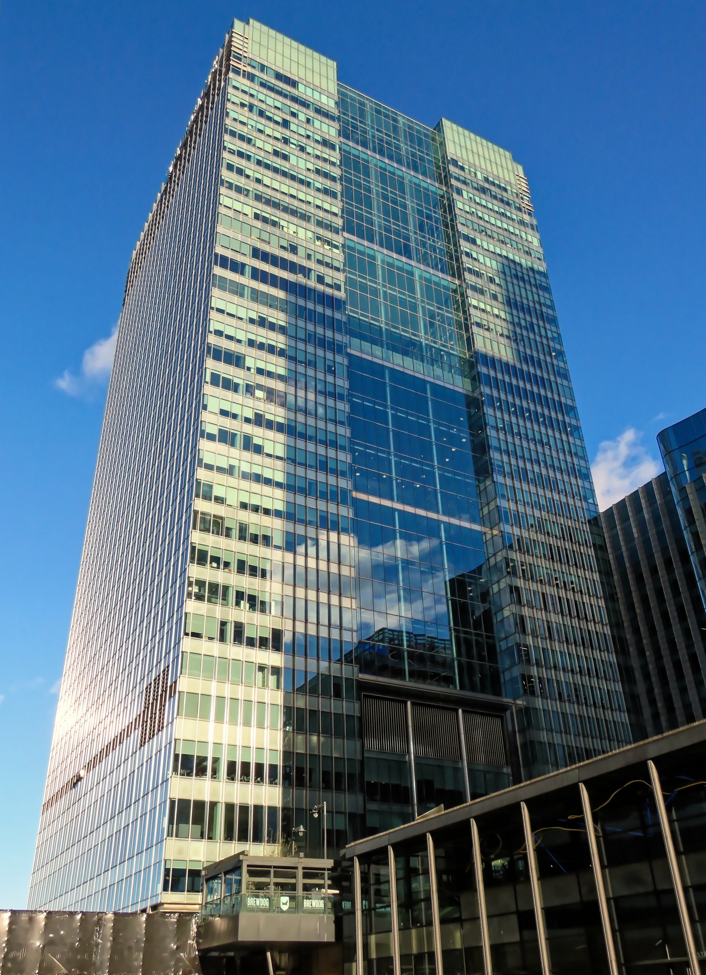 Barclays global headquarters at One Churchill Place in Canary Wharf, London, with the Barclays name and eagle logo above the entrance and office workers below