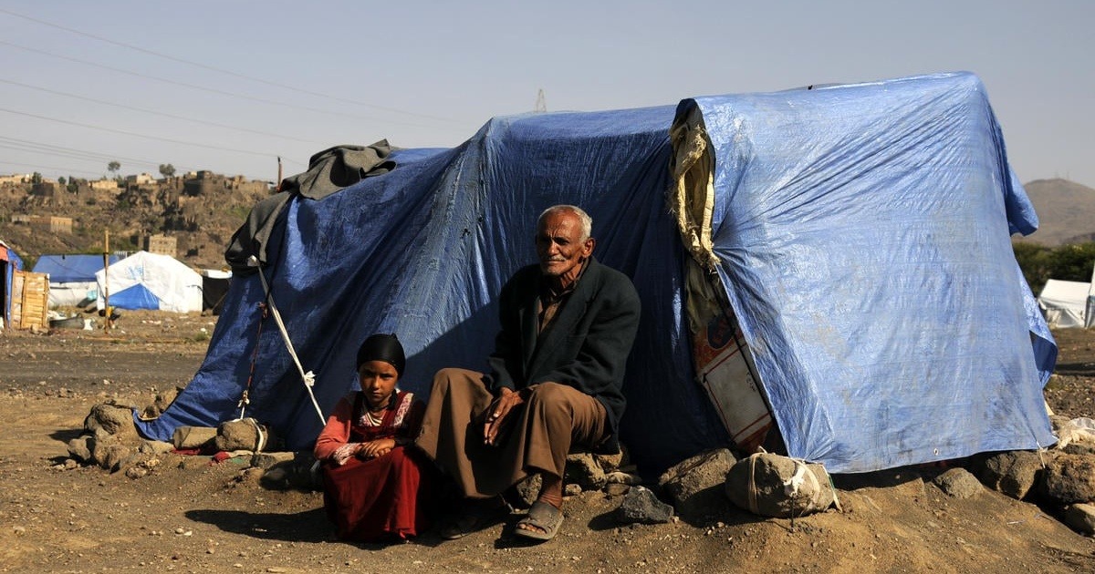 A displaced Yemeni man and child sit outside a temporary shelter