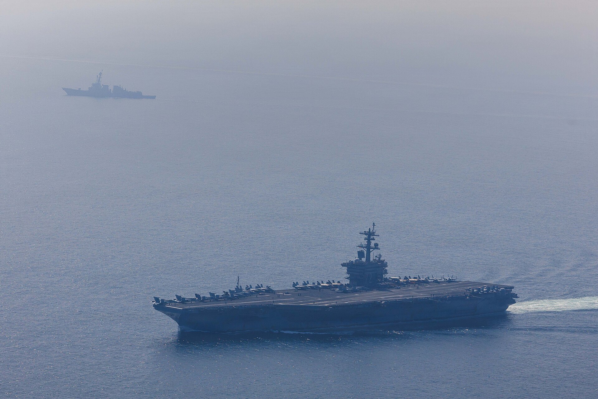 The aircraft carrier USS Abraham Lincoln underway at sea with a carrier strike group escort visible in the haze — a US carrier strike group Middle East November 2026 deployment in an earlier rotation