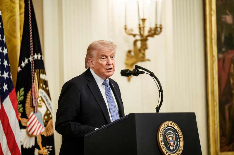 President Donald Trump at a White House podium as Trump blames Ukraine for gas prices