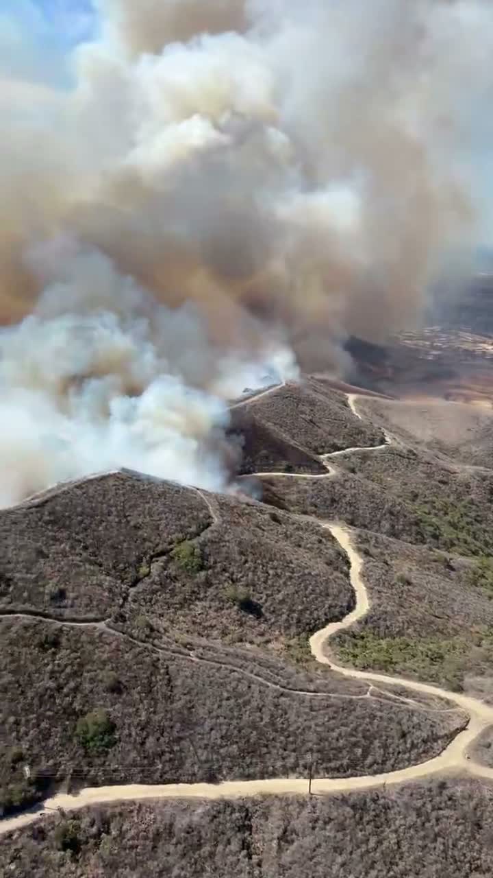 A column of smoke rises from the Norte Fire burning through brush hills above San Clemente, seen from a firefighting helicopter