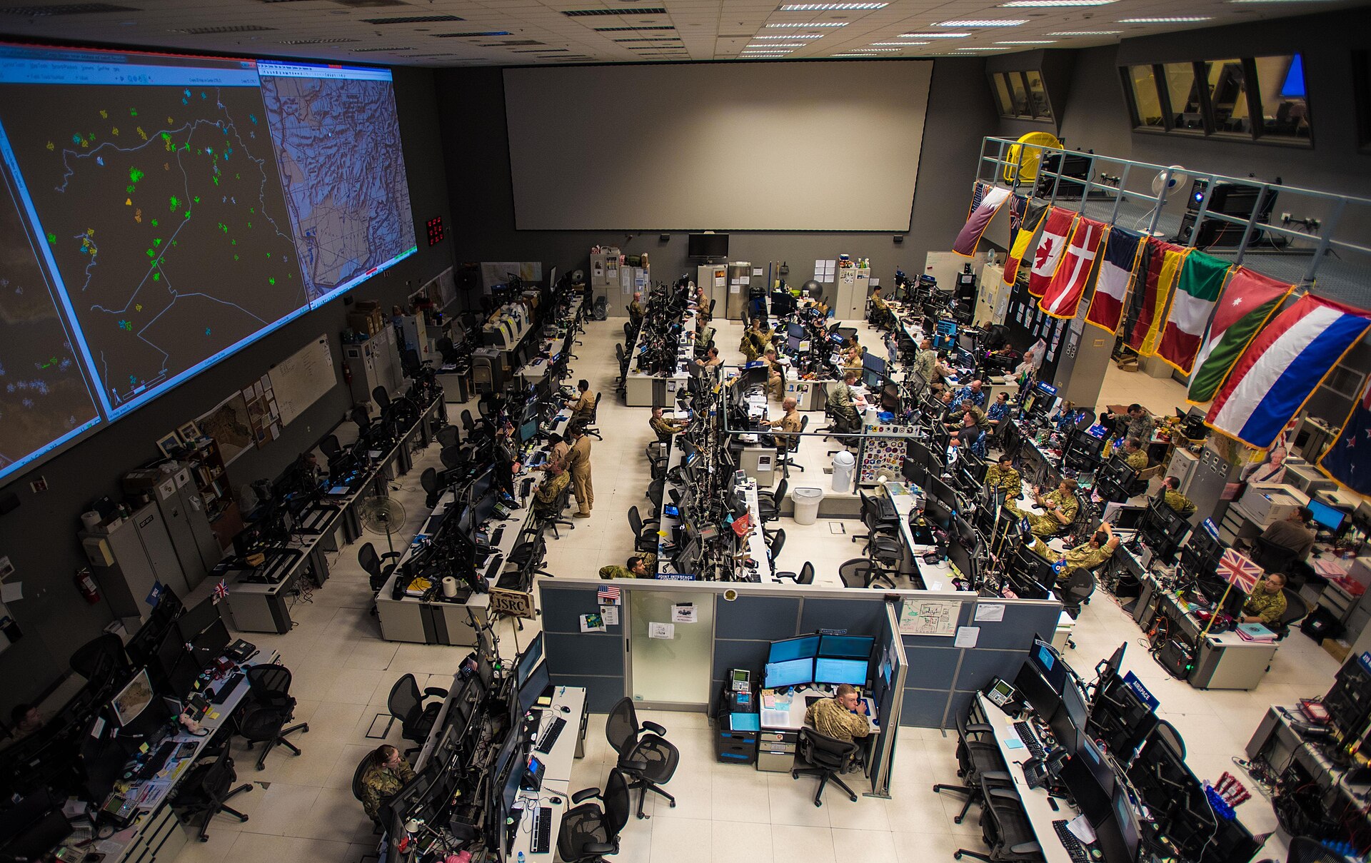 Inside the Combined Air Operations Center at Al Udeid Air Base in Qatar, where coalition personnel under the flags of partner nations coordinate air operations across the region