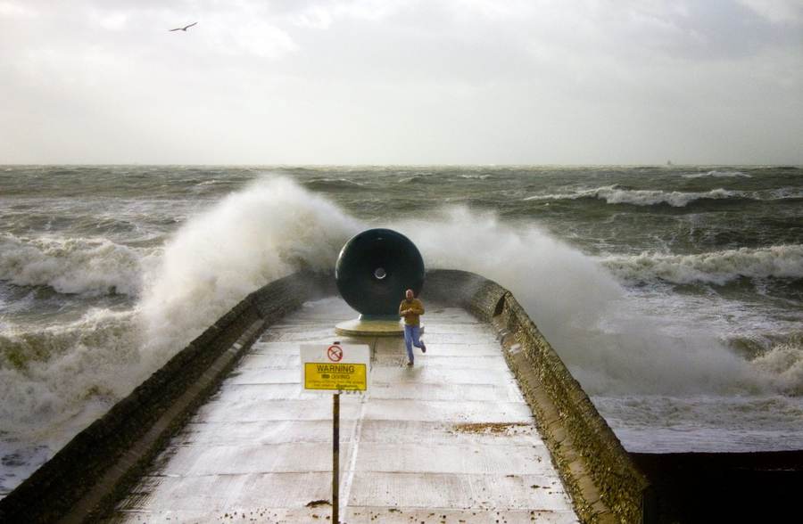 Large storm-driven waves striking a coastal breakwater, illustrating the dangerous surf behind East Coast festival cancellations