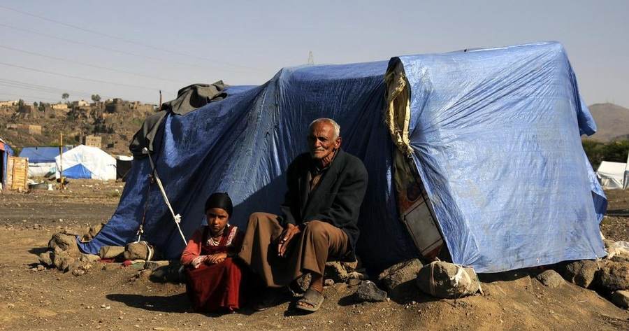 A displaced Yemeni man and child sit outside a temporary shelter