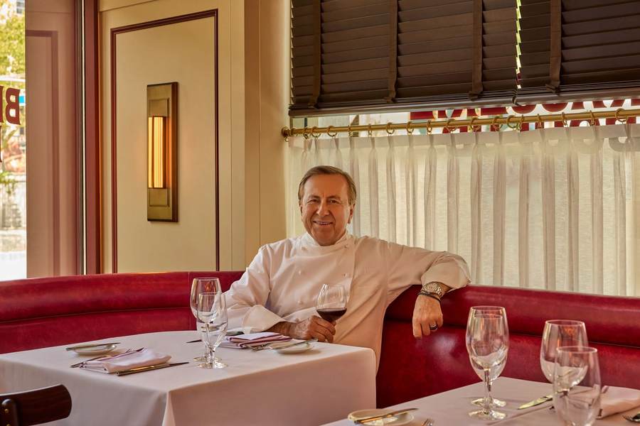 Chef Daniel Boulud seated in a red banquette inside Brasserie Boulud on the Upper West Side