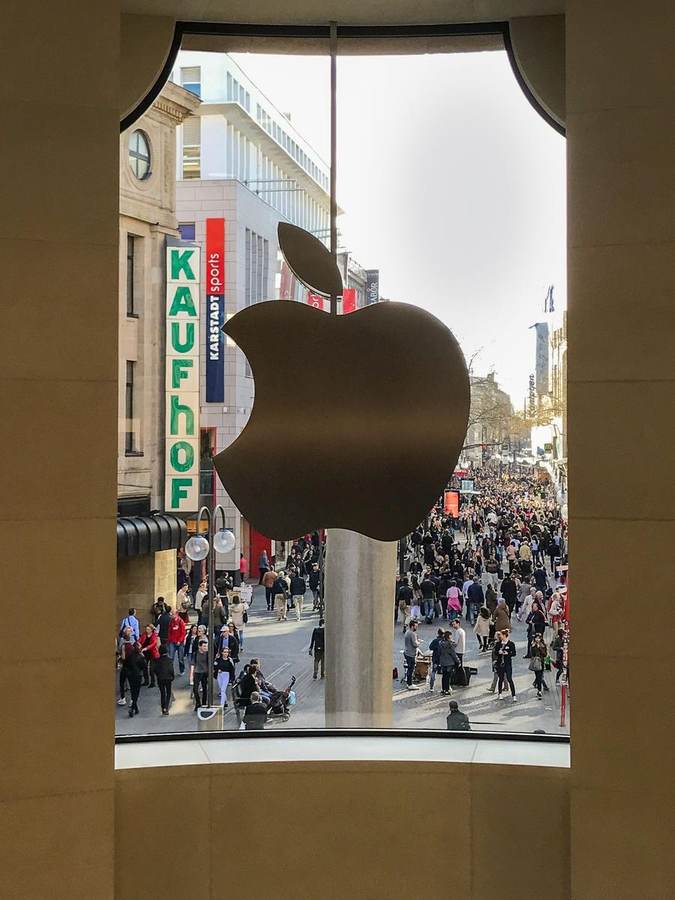 Apple logo on the glass facade of the Apple Store in Cologne, Germany, overlooking a busy shopping street