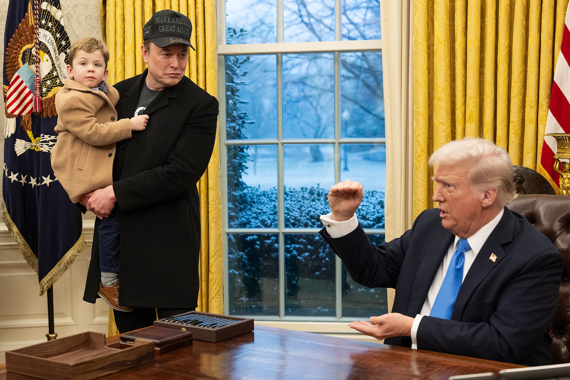 President Donald Trump seated at the Resolute desk in the Oval Office with Elon Musk standing beside him, February 2025