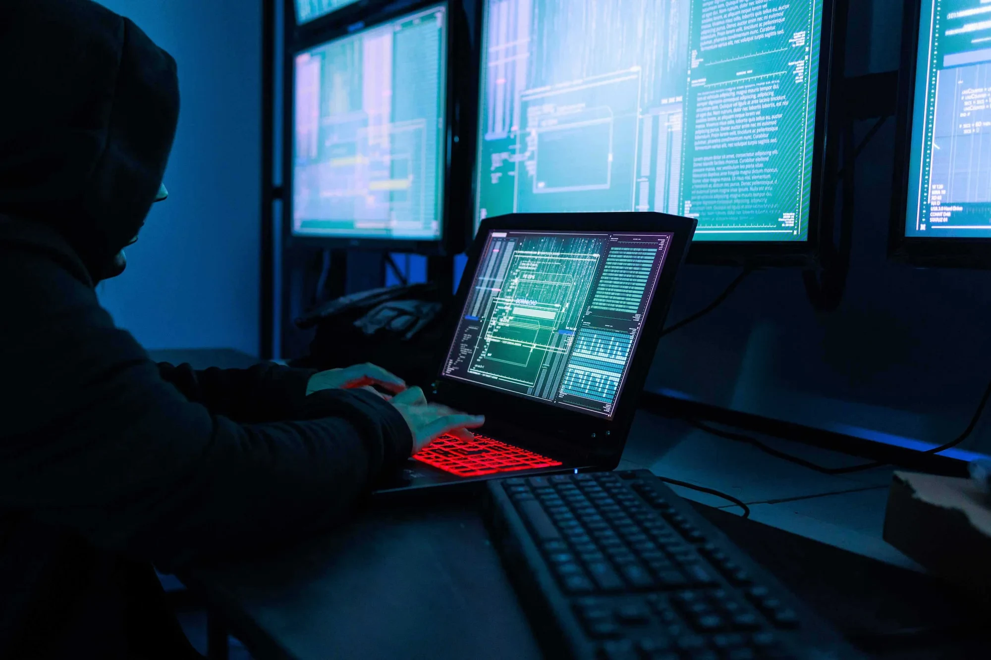 A hooded figure at computer monitors — NorForge identified more than 20 exposed Cairn panels it assesses as likely connected to malicious operations, file photo