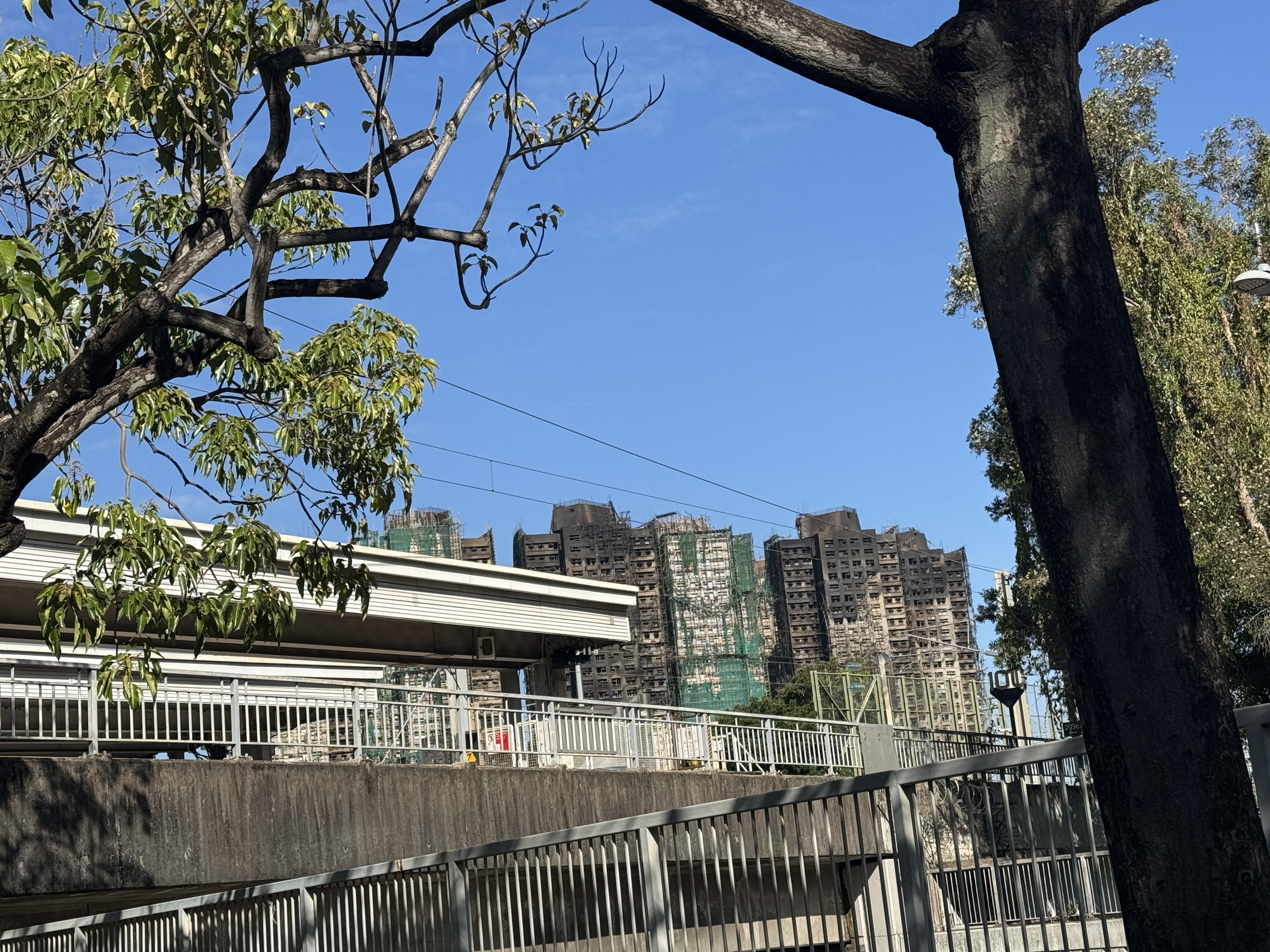 The blackened towers of Wang Fuk Court in Tai Po seen three days after the Hong Kong fire that killed 168 people, with burnt scaffolding and green netting still on the buildings