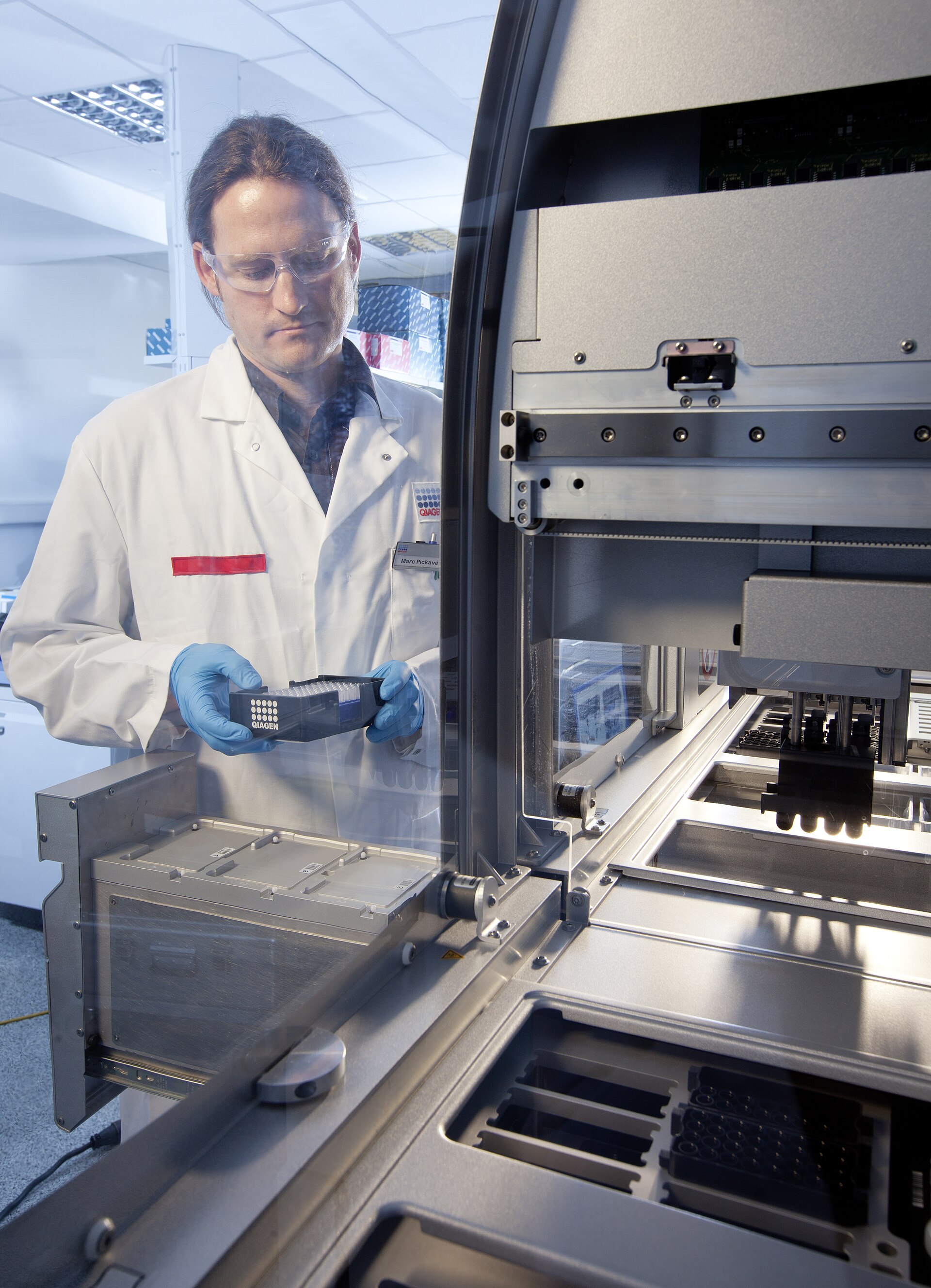 A technician holding a Qiagen sample tray beside a QIAsymphony automation system — Qiagen takeover offer