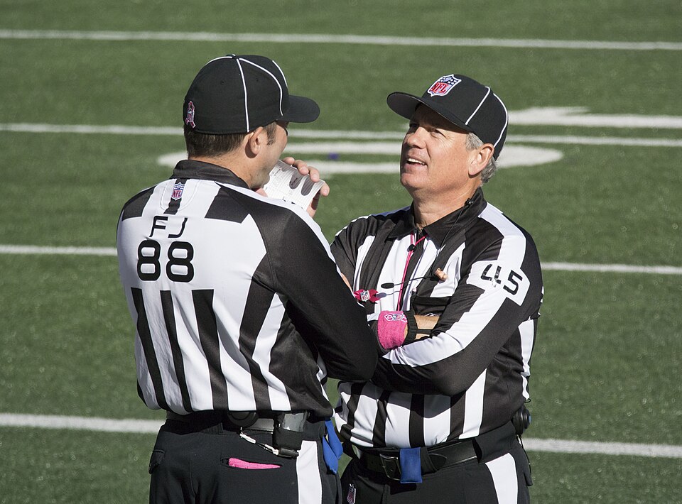 Two NFL officials in black-and-white uniforms conferring on the field