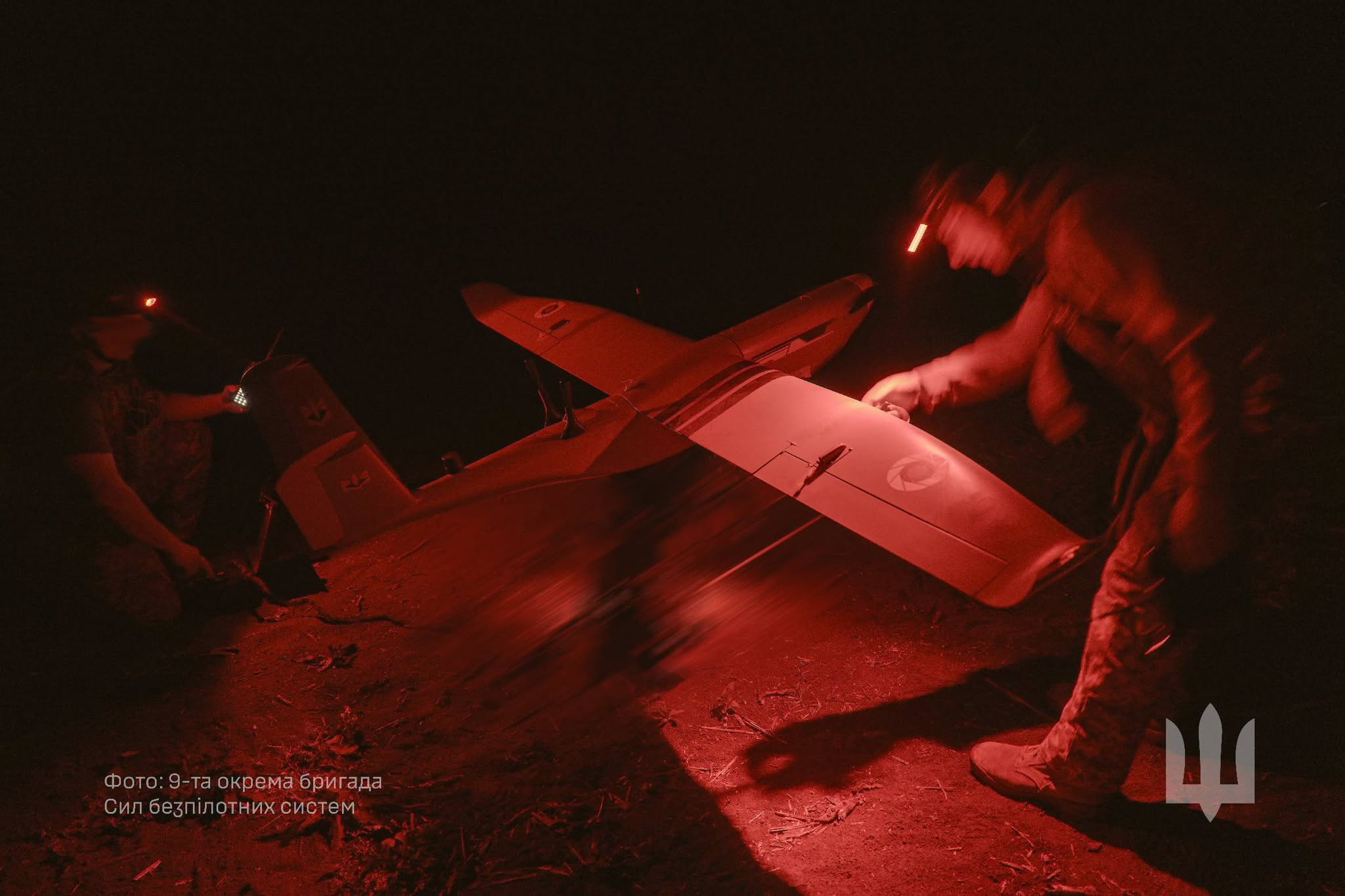 Ukrainian soldiers of the 9th Separate Unmanned Systems Brigade prepare a fixed-wing attack drone at night under red light