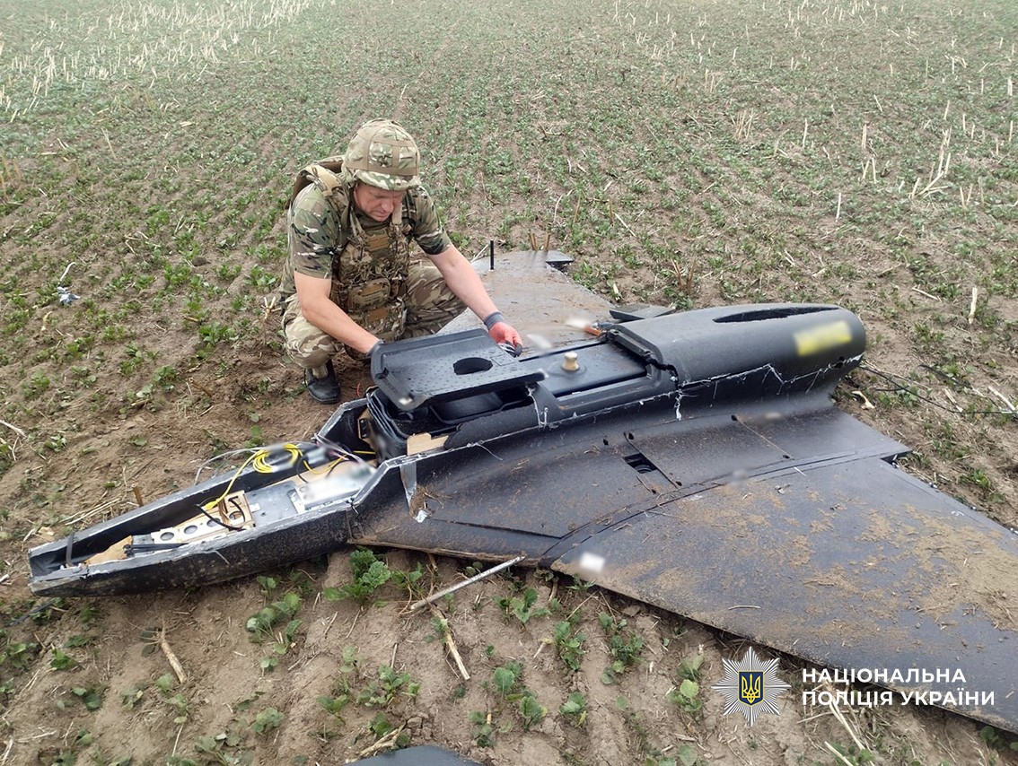 A Ukrainian police explosives specialist examines the wreckage of a downed Geran Shahed-type drone in a field — Kharkiv park drone strike file photograph