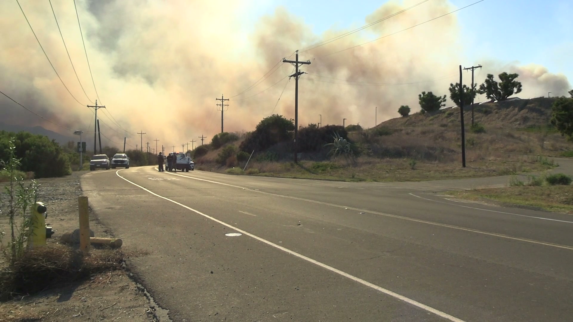 A towering smoke column from the Henderson Fire rises over a Camp Pendleton road as emergency vehicles stage below on October 15, 2026