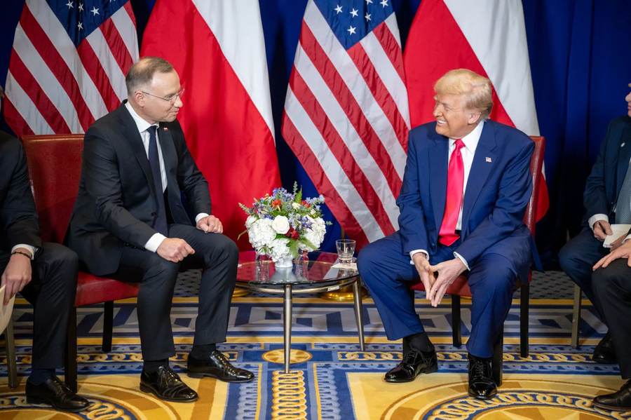 Donald Trump and former Polish President Andrzej Duda sit together during a meeting framed by American and Polish flags