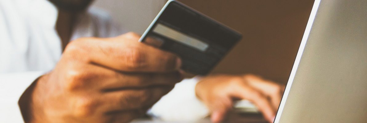 Online shopper holding a payment card beside a laptop