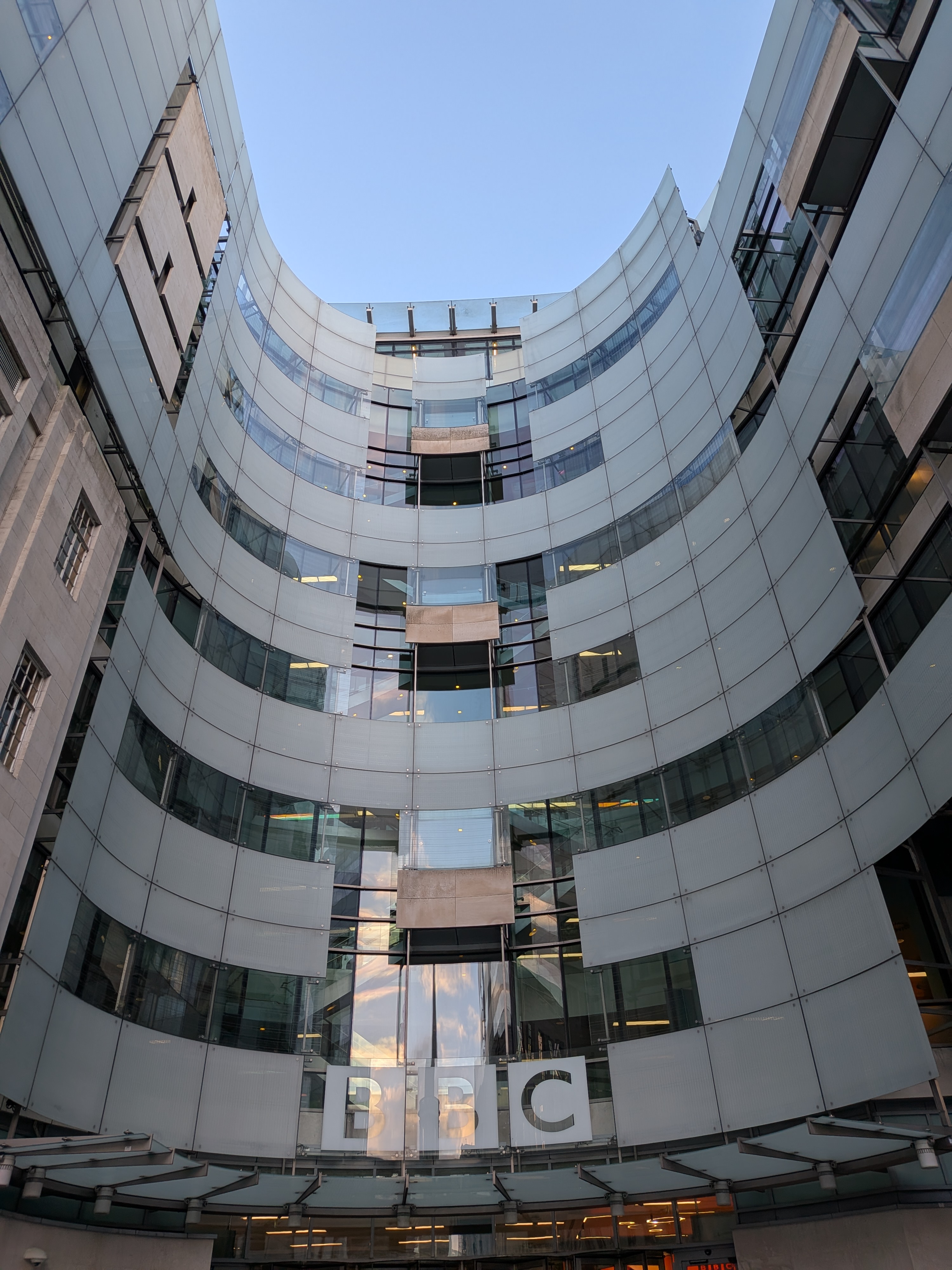 BBC defamation lawsuit $10 billion — the curved glass front of Broadcasting House, the BBC's London headquarters, with the BBC block letters above the entrance