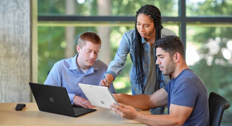 People collaborating around a Microsoft Surface laptop, illustrating the workplace setting for the new Copilot Home, Code and Autopilot tools