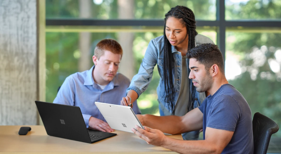 People collaborating around a Microsoft Surface laptop, illustrating the workplace setting for the new Copilot Home, Code and Autopilot tools