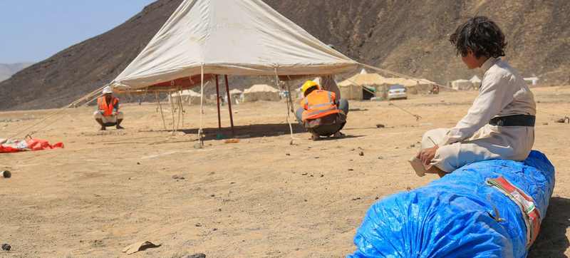A displaced Yemeni child watches IOM workers erect emergency shelter during the Yemen displacement crisis