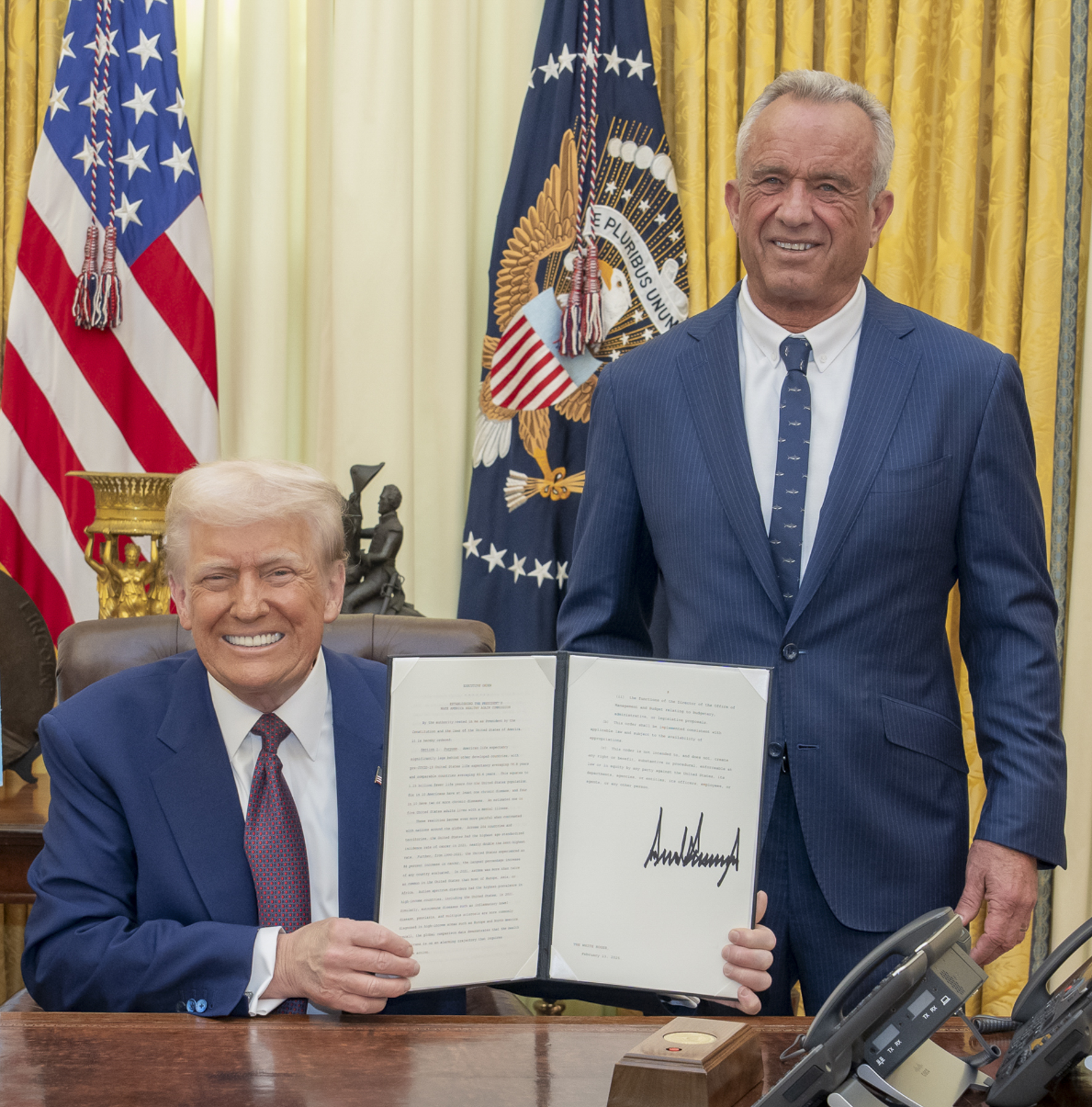President Donald Trump with Health Secretary Robert F. Kennedy Jr. holding the signed Make America Healthy Again Commission order in the Oval Office, February 2025