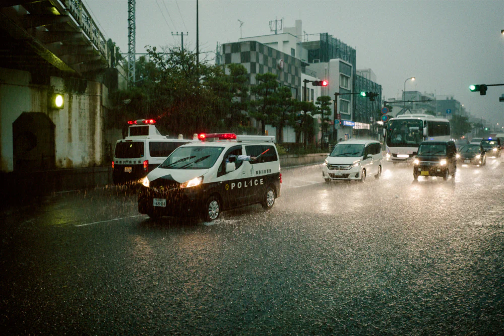 Police and other vehicles driving through intense rain in Kamakura during Typhoon No. 15 in September 2025