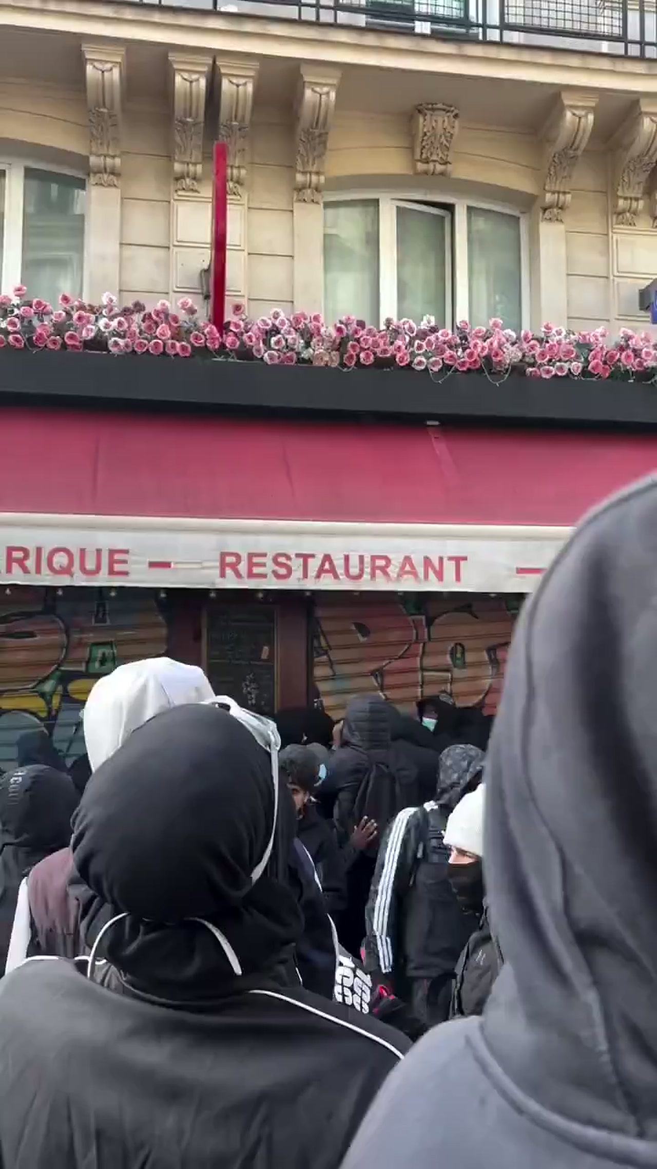 People in the crowd pointing up at the balcony and filming with phones outside La Barrique café in Paris during the riots